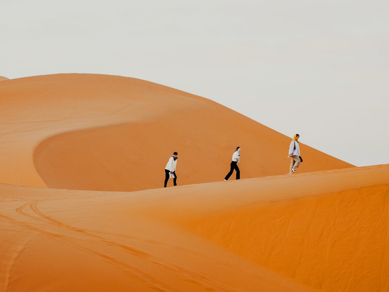 brand-01 Three individuals walking on the vast orange sand dunes in Marrakesh, Morocco
