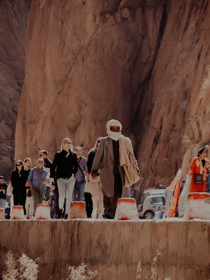 Group of tourists with a desert guide walking through a canyon in Marrakesh, Morocco under bright sunlight.